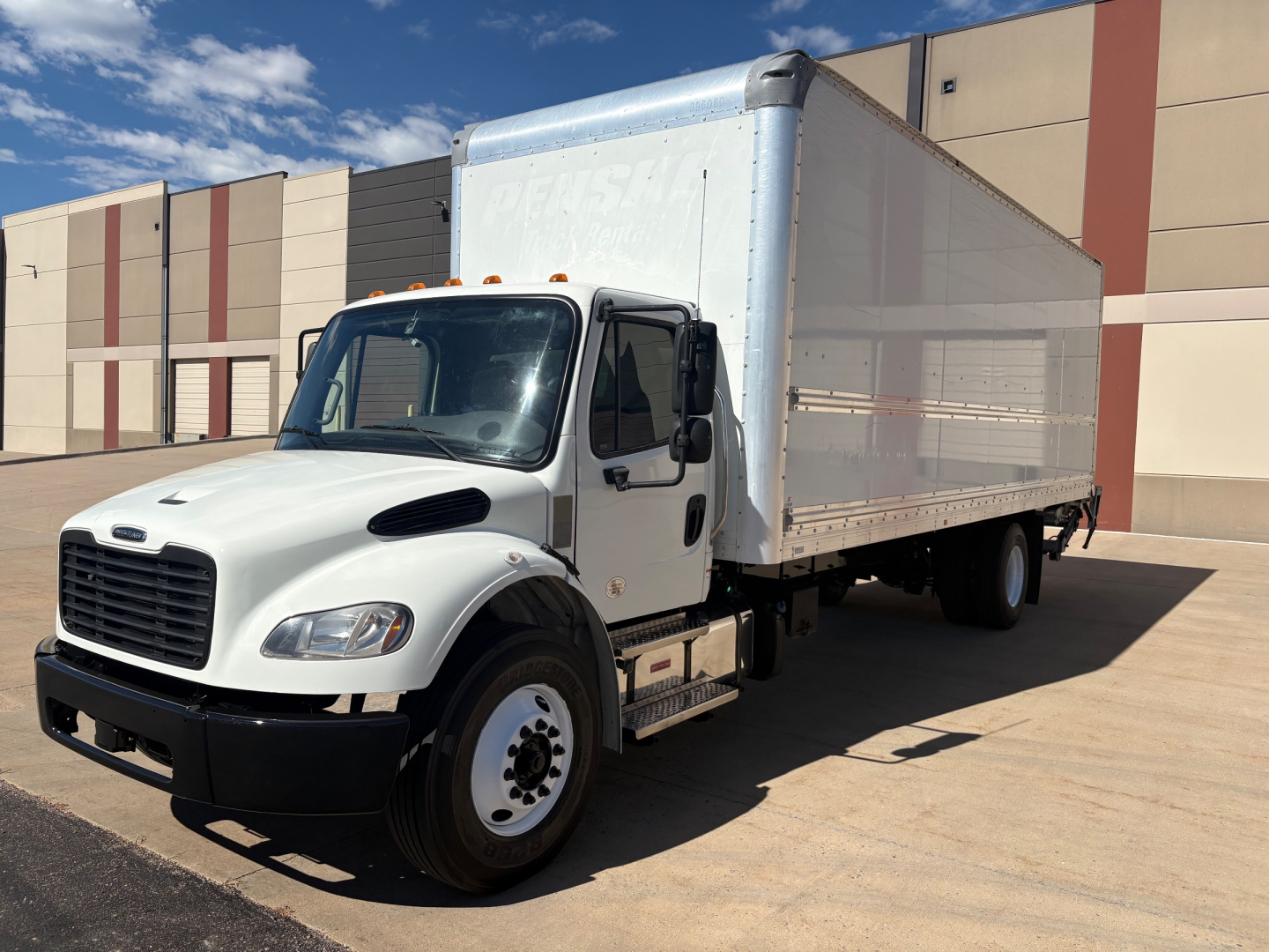 Freightliner M2-106 box truck in white cab with a large aluminum cargo box, front view at an industrial lot.