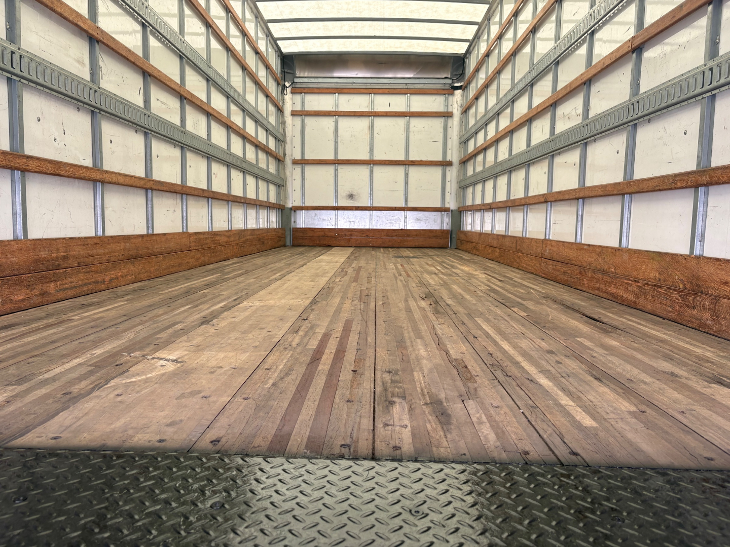 Truck bed interior of a Freightliner M2-106 box truck showing wooden flooring and metal side walls.