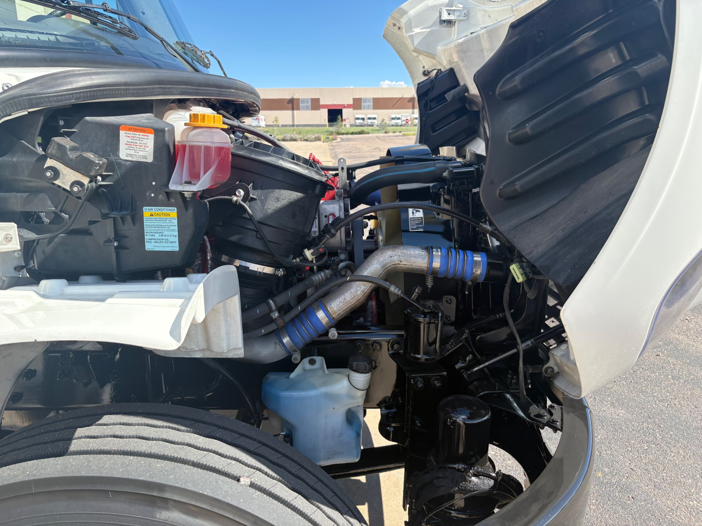 Front engine bay of a 2022 Freightliner M2-106 showing coolant reservoir, power steering reservoir, hoses, and various components in view.
