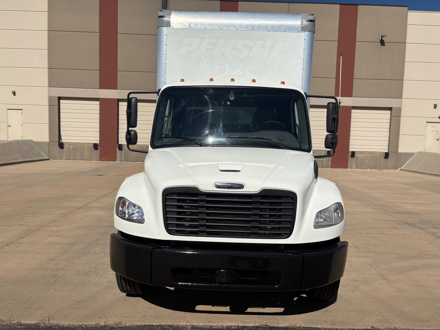 Freightliner M2-106 box truck front view. White cab, black grille and bumper, large side mirrors. Cargo box visible behind cab.