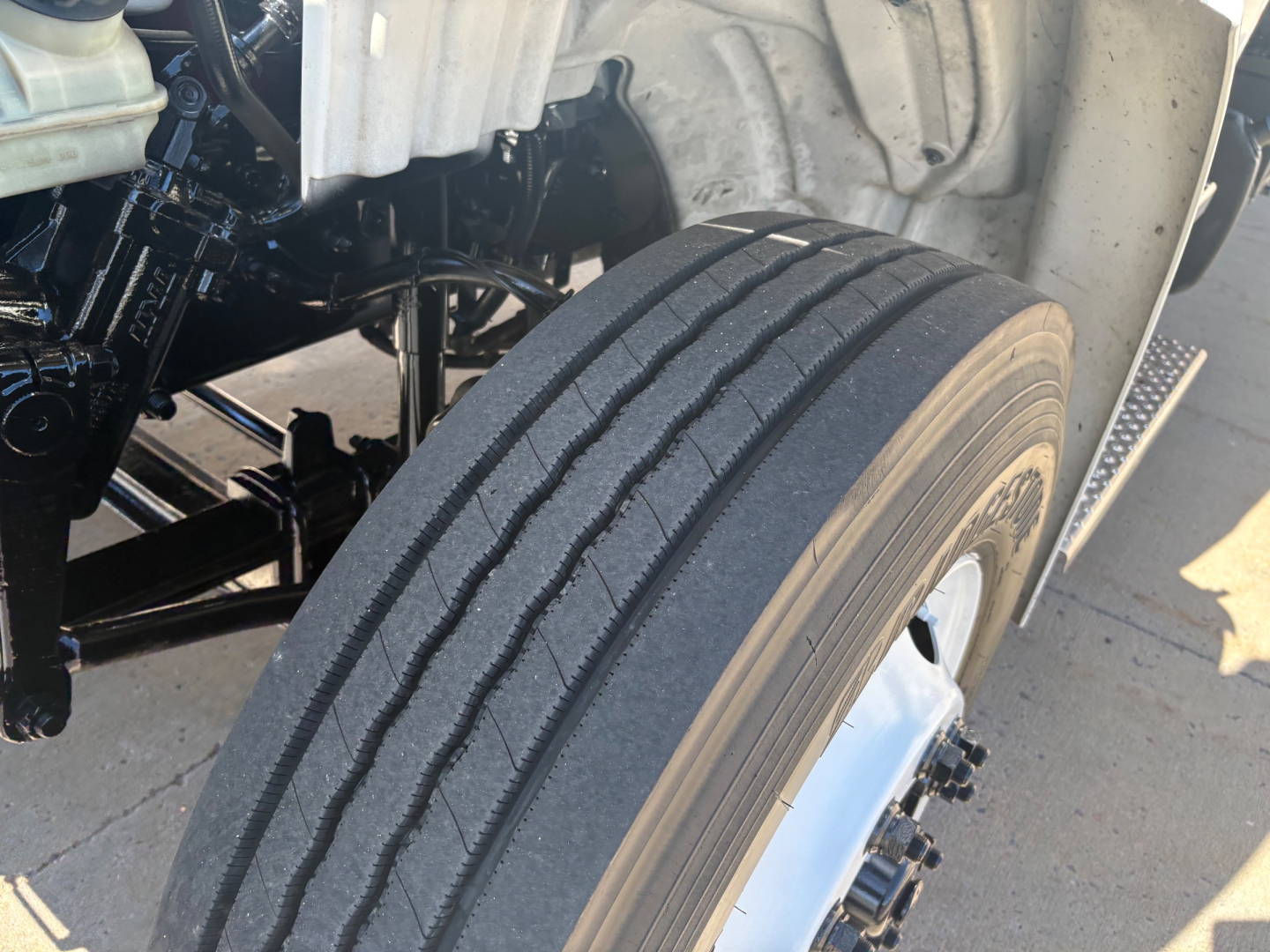 Truck front wheel and suspension visible in a Freightliner M2-106, with tire tread and wheel rim in view.
