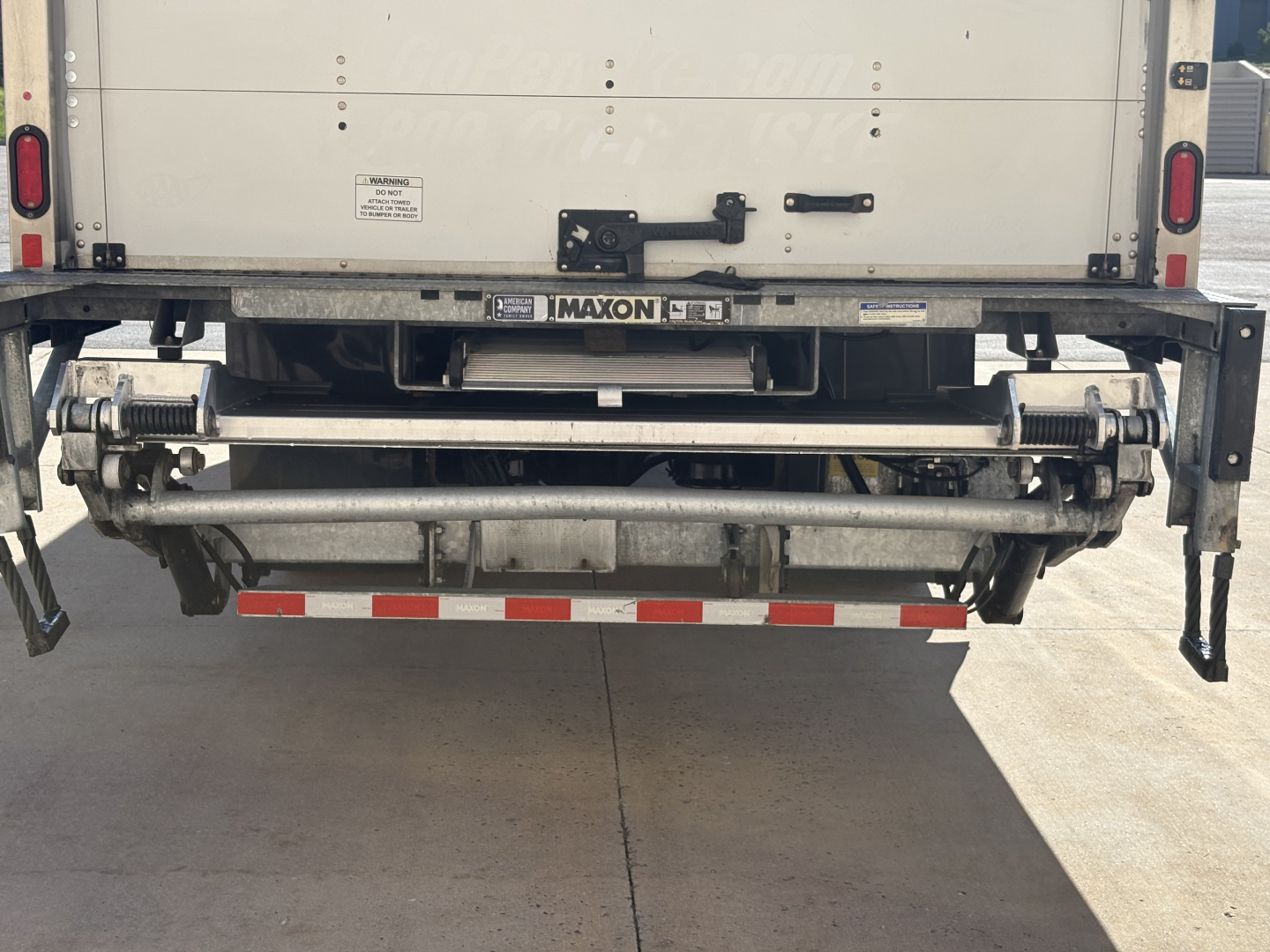 Rear view of Freightliner M2-106 dump truck showing Maxon rear suspension or bumper assembly and hydraulic lines.
