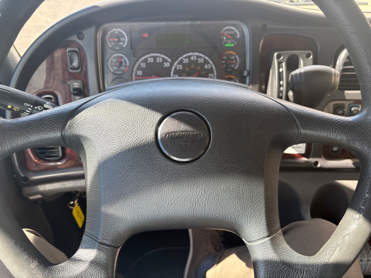 Freightliner M2-106 cab interior showing steering wheel with Freightliner emblem and dashboard gauges in view.