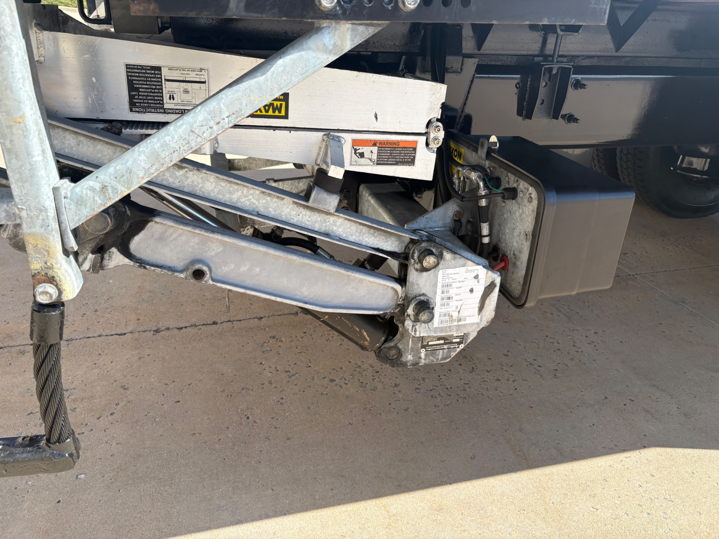 Freightliner M2-106 side view undercarriage with stabilizer jack and hydraulic lift components visible, shows metal framework and warning labels.