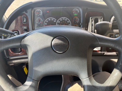 Freightliner M2-106 cab interior showing steering wheel with Freightliner emblem and dashboard gauges in view.