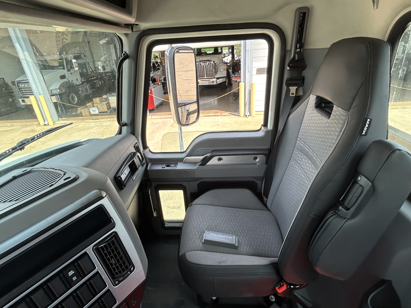 Cab interior of a 2027 Mack GR64F crane truck showing driver seat, dashboard, and side window with door mirror; VIN and stock info not visible in image.