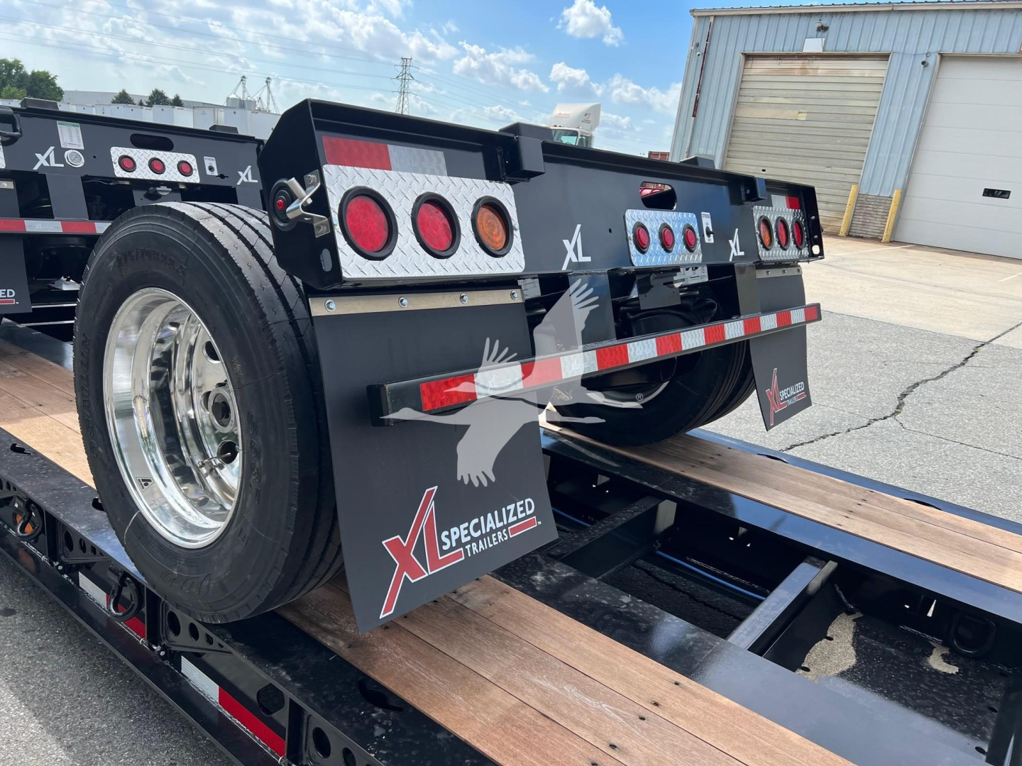 XL Specialized XL22Fa lowboy trailer showing rear deck and spare tire mounted on left side with tail lights and reflective safety stripe.