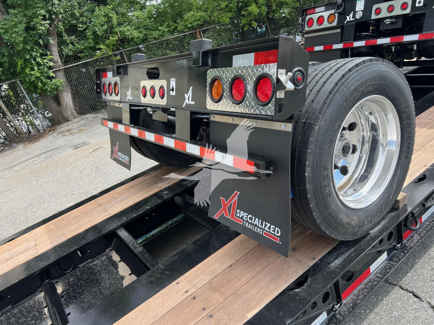 Trailer rear view showing XL Specialized branding, taillights, mud flaps, and a wood deck on a lowboy trailer; wheel and trailer frame visible.