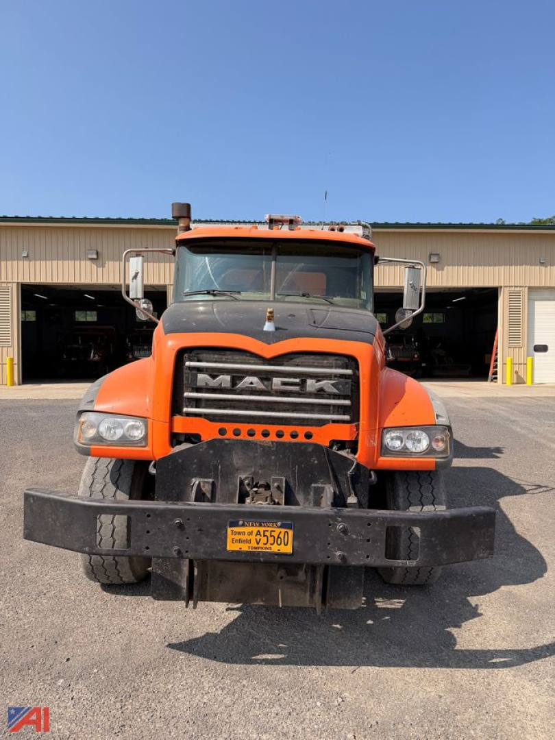 Front view of a 2008 Mack GU713 dump truck with plow and wing, orange cab, large grille, license plate visible on front bumper.