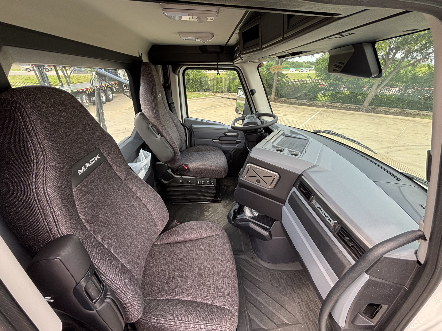 Interior cab of a 2027 Mack AN64T daycab with gray fabric seats, steering wheel, dashboard, and center console visible.