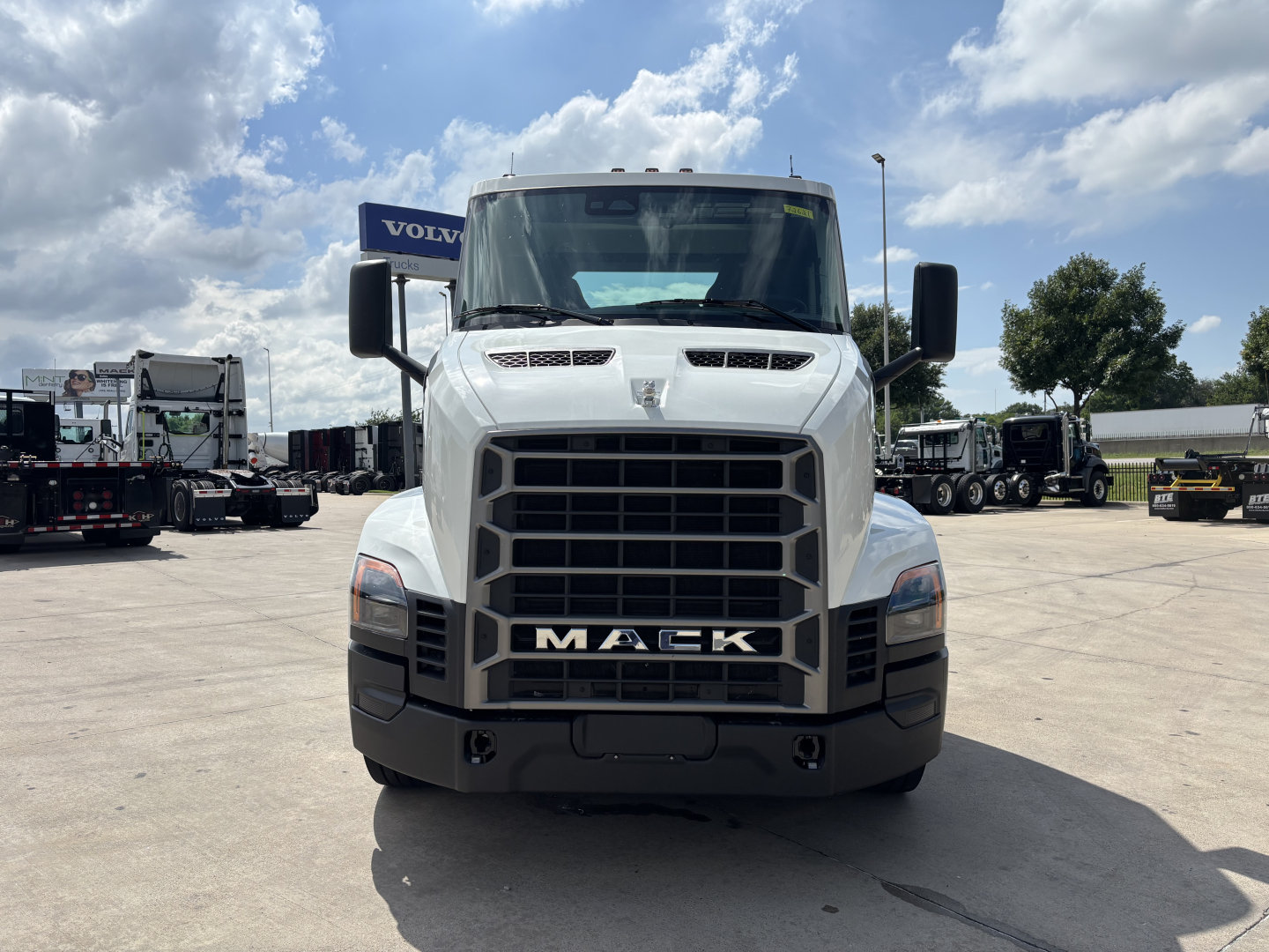 Mack AN64T truck front view showing large grille, headlights, and 'MACK' emblem on the bumper in a dealership lot.