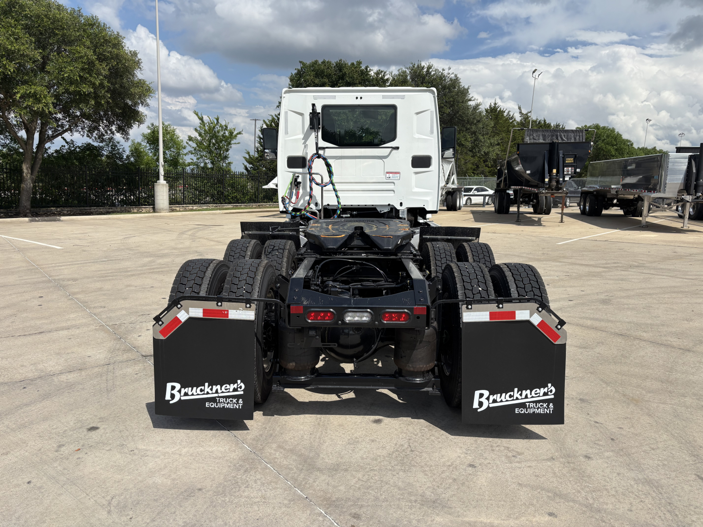 S rear view of a white Mack AN64T daycab truck tractor, chassis and dual rear axles, mudflaps labeled "Bruckner's Truck & Equipment" in a parking lot.