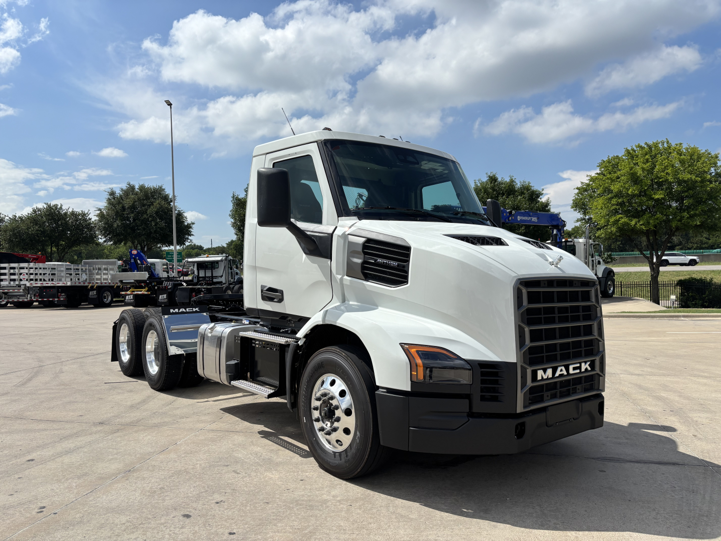 Mack AN64T conventional daycab truck in a dealership lot with white cab and black grille, side view showing 6-wheel configuration and front badge reading MACK