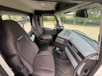 Interior cab of a 2027 Mack AN64T daycab with gray fabric seats, steering wheel, dashboard, and center console visible.