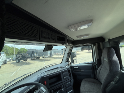 Truck cab interior of a 2027 Mack AN64T showing dashboard, steering wheel, and seating with overhead storage and sun visors.