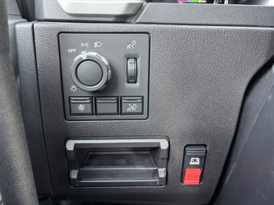 Dashboard control panel of a 2027 Mack AN64T showing headlight dial, rotary dimmer, and five switch buttons; small cubby and a red 'Save' button on the right.