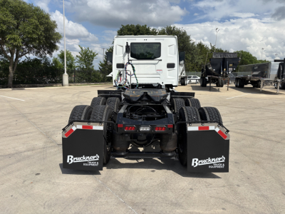 S rear view of a white Mack AN64T daycab truck tractor, chassis and dual rear axles, mudflaps labeled "Bruckner's Truck & Equipment" in a parking lot.