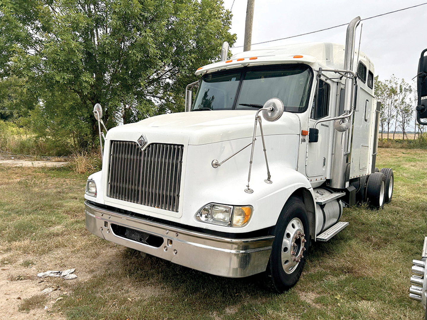 International 9400i conventional sleeper truck showing chrome grille, large hood, dual chrome exhaust stacks, white cab, front left view