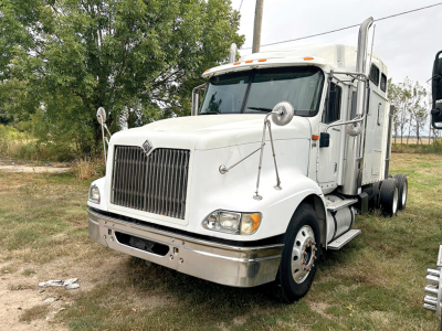 International 9400i conventional sleeper truck showing chrome grille, large hood, dual chrome exhaust stacks, white cab, front left view