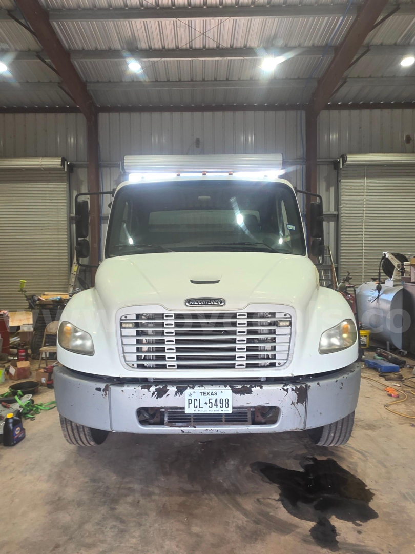 Front view of a white 2008 Freightliner M2 106 truck inside a garage, with a Texas license plate and a spill on the ground, stock number 31912-16.