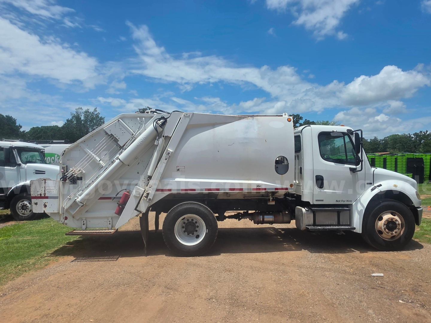Garbage truck side view showing a rear compactor body mounted on a Freightliner M2 106 chassis with white cab and side loader arm.