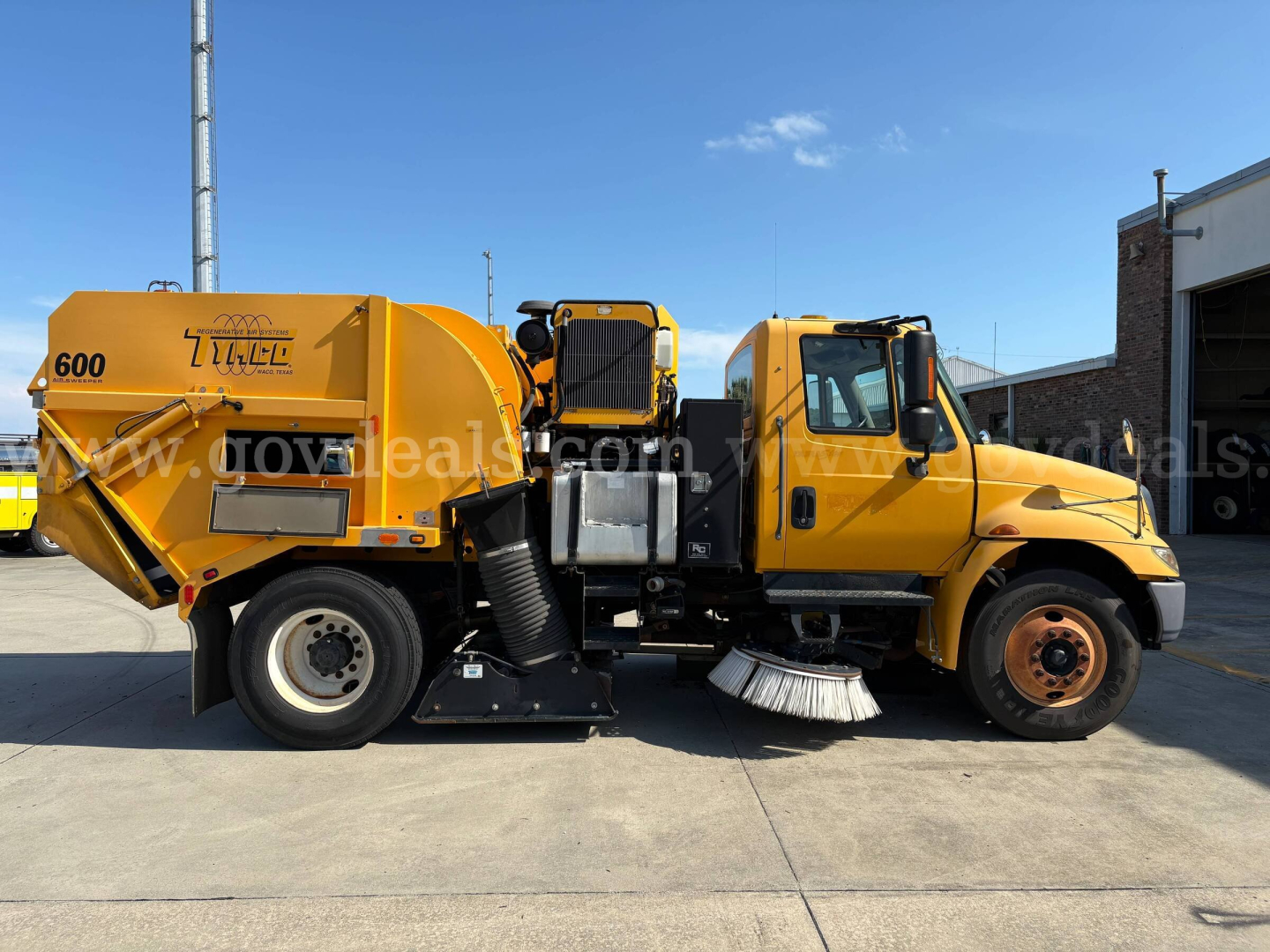 International 2012 DuraStar street sweeper truck shown in side profile with yellow cab and body, 600 label on rear, sweeping brush visible under cab, VIN and stock not visible.