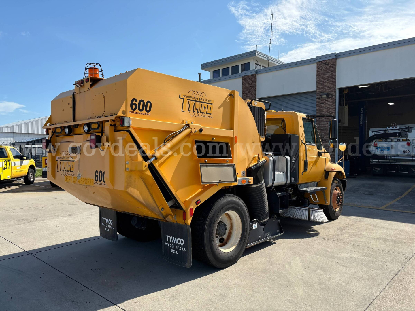 Truck rear and side view of a yellow 2012 International DuraStar street sweeper showing rear waste hopper and dual rear tires.