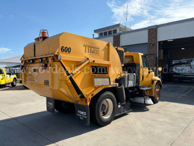 Truck rear and side view of a yellow 2012 International DuraStar street sweeper showing rear waste hopper and dual rear tires.