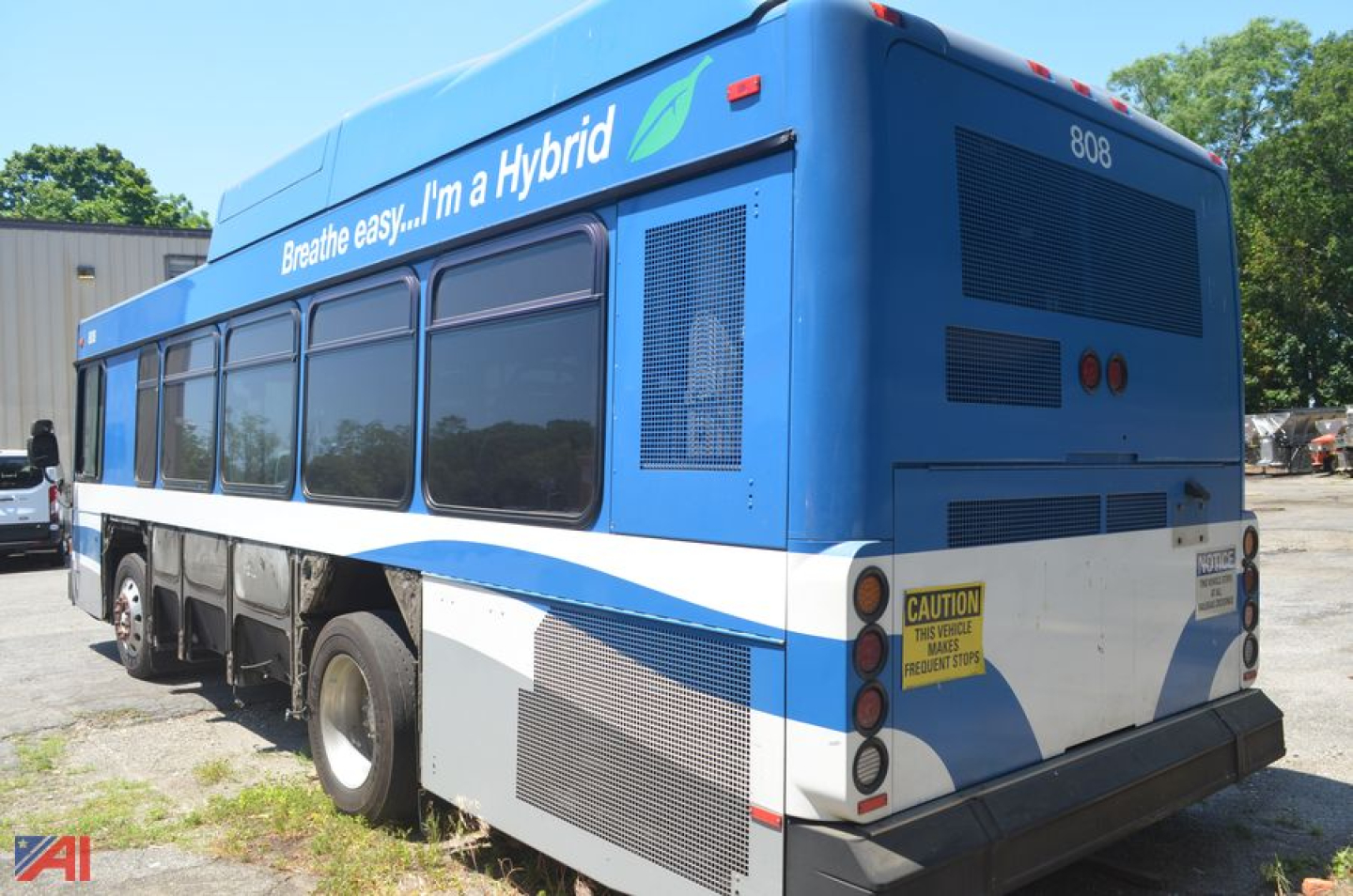 Bus rear view showing hybrid branding and spare tire area on Gillig Low Floor bus, side windows, blue and white livery, caution sticker, rear vents.