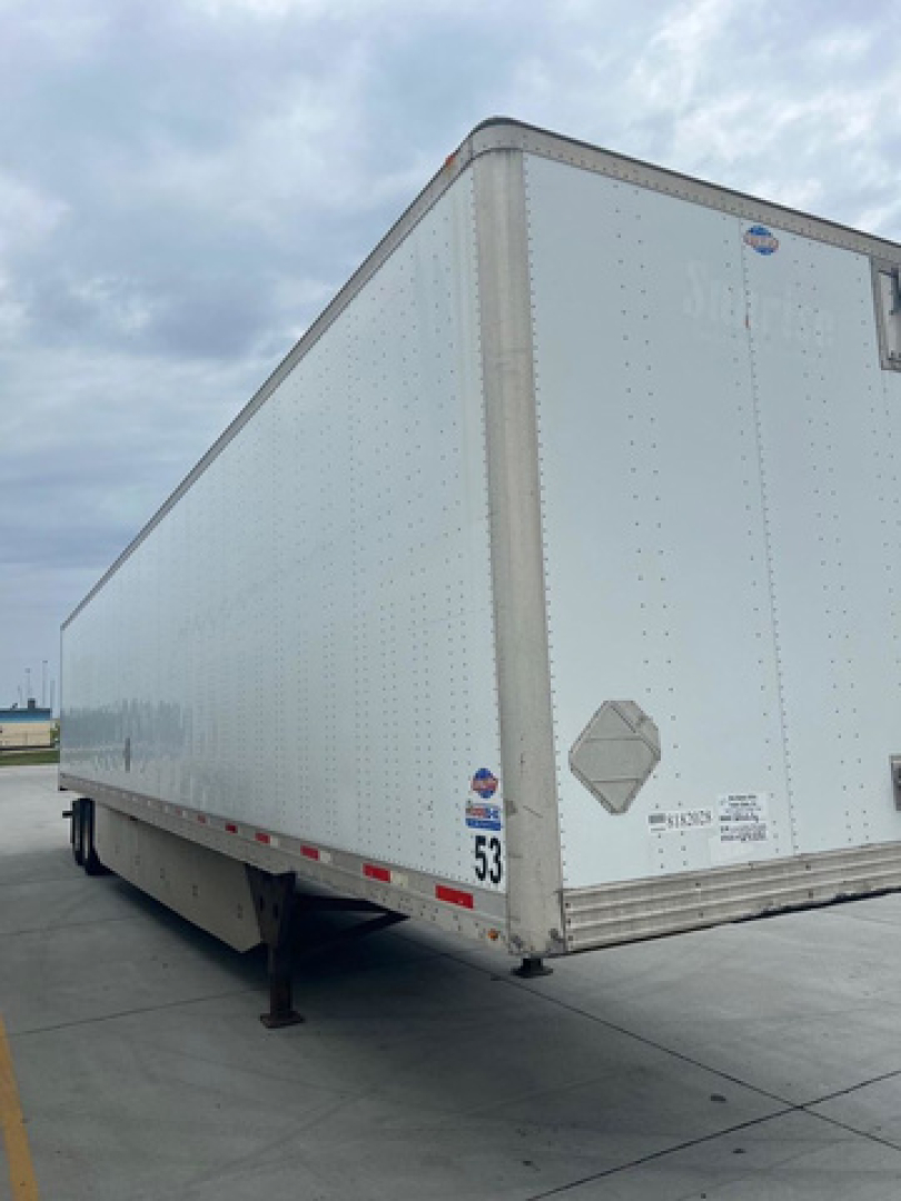 Trailer side view of a 2014 utility van trailer showing a long aluminum cargo box with support legs extended, load rating stickers and a safety diamond plate near rear.