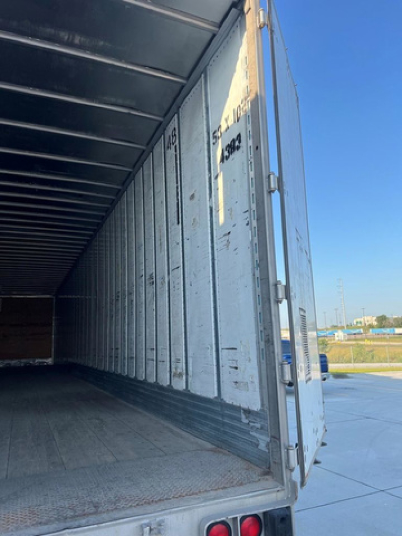 Interior of a light gray/metallic trailer with open rear, showing side wall panels with wear marks and a diamond-plate floor. Exterior shows vertical seams and rear door.