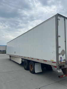 Utility van trailer showing long white box trailer with tandem rear axles and mud flaps.