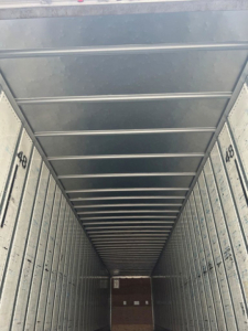 Van trailer interior cargo space with metal sidewalls and ceiling, long narrow perspective, numbered panels along walls.