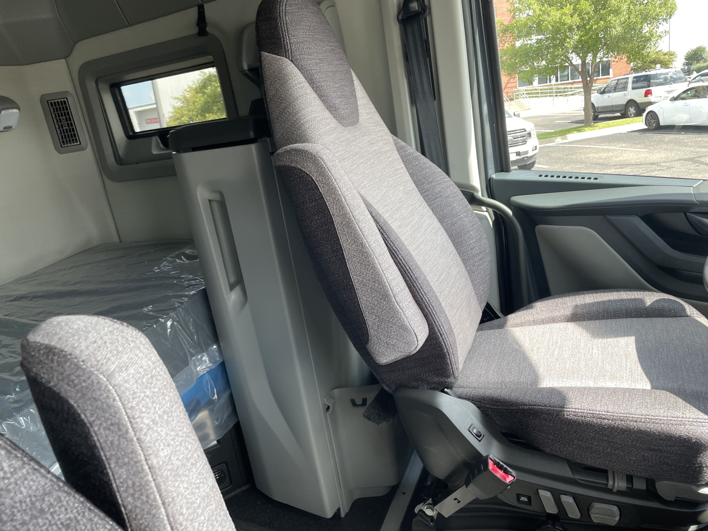 Volvo VNL64T660 cab interior view showing driver seat and sleeper area, grey fabric seats, dashboard edge, and window.