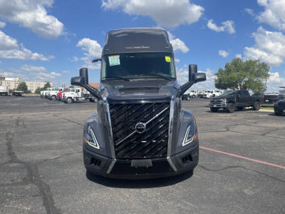 Volvo VNL64T660 truck front view showing bold grille, headlights, and Volvo emblem; daytime outdoor lot with other trucks in background.