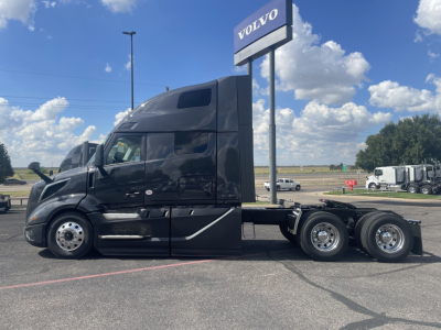 Volvo VNL64T660 semi-truck tractor in black, side profile view, with Volvo sign in background.