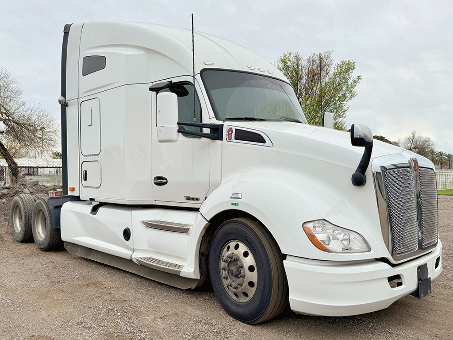 Kenworth T680 sleeper cab tractor in white, side view showing front grille, windshield, and dual rear axles.