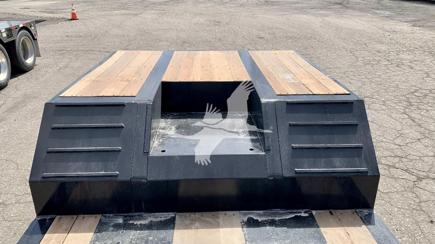 Front view of a Fontaine Renegade N12 lowboy trailer deck with wooden planks and black protective sides, center cut-out, and ramps/stowage areas.