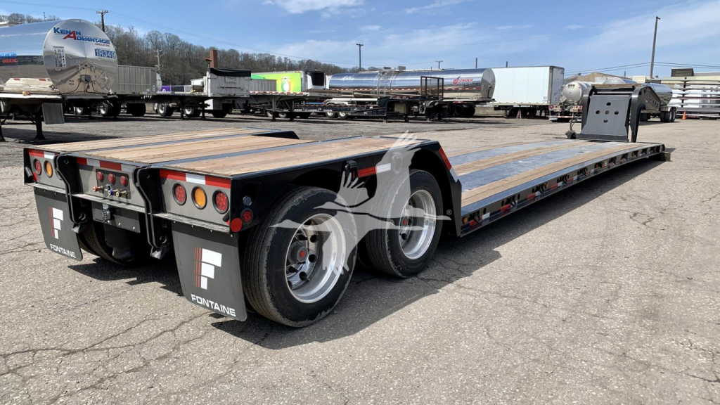 Fontaine Renegade N12 lowboy trailer showing dual rear axles, wooden deck, taillights, and landing gear with stock number V35A7294 visible.