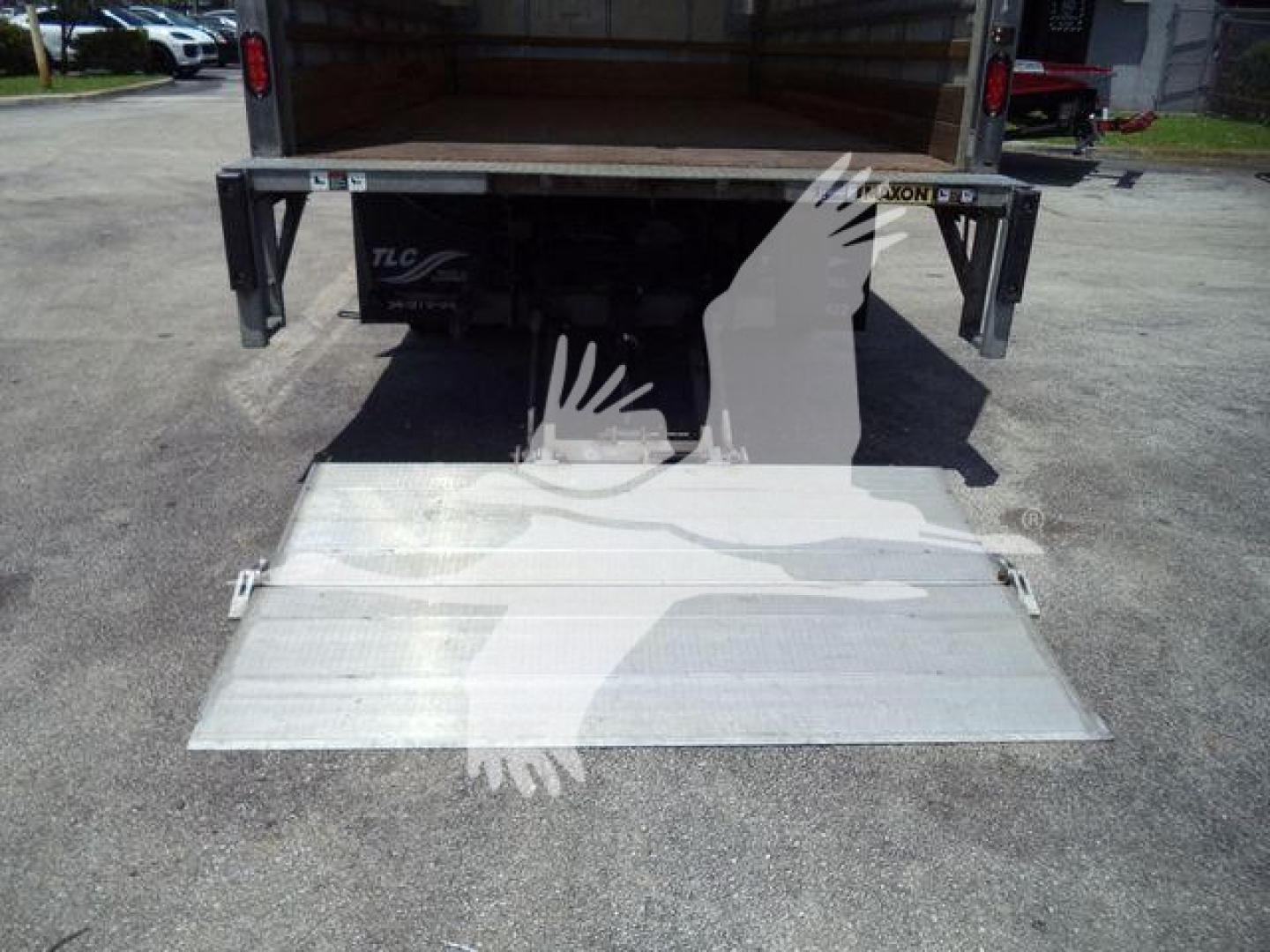 Isuzu NPR-HD box truck rear with unfolded aluminum ramp and open cargo area.