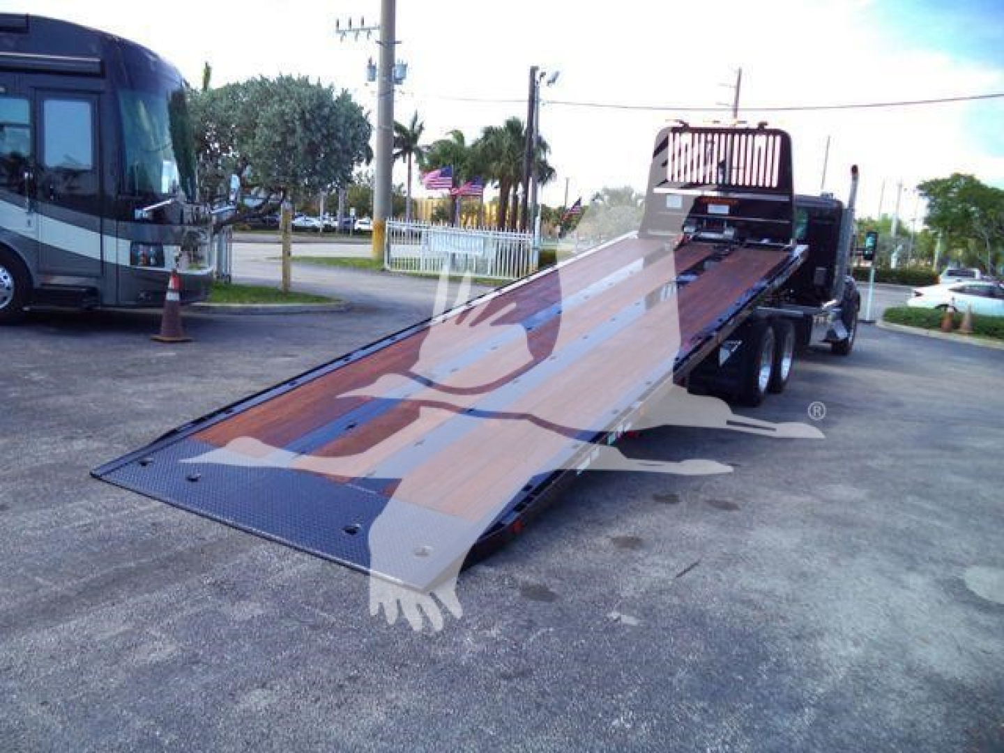 Truck flatbed rollback showing a Kenworth T880 part or accessory with a metallic loading ramp extended, in a dealership lot.