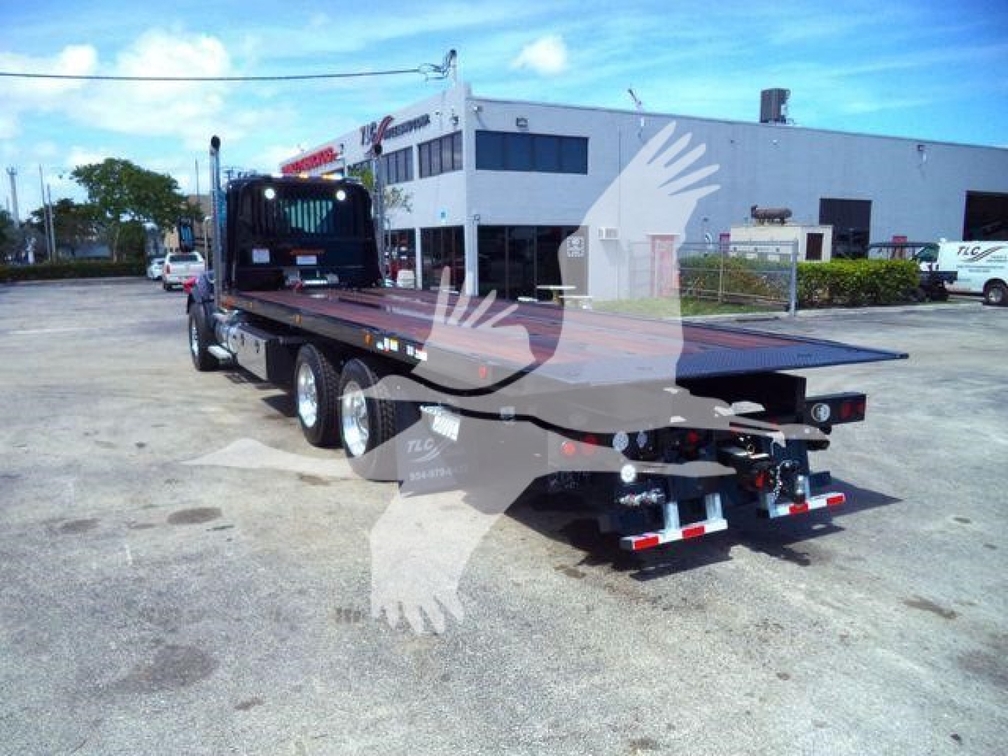 Kenworth T880 rollback truck with flatbed trailer in a dealership lot, rear view showing dual rear axles and equipment hitch.