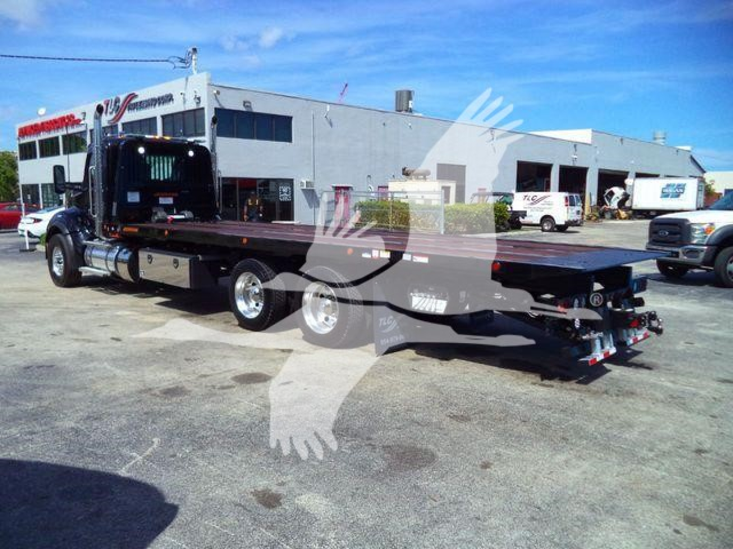 Kenworth T880 rollback truck with flatbed, side view showing long flatbed and rear controls, set against a dealership lot.