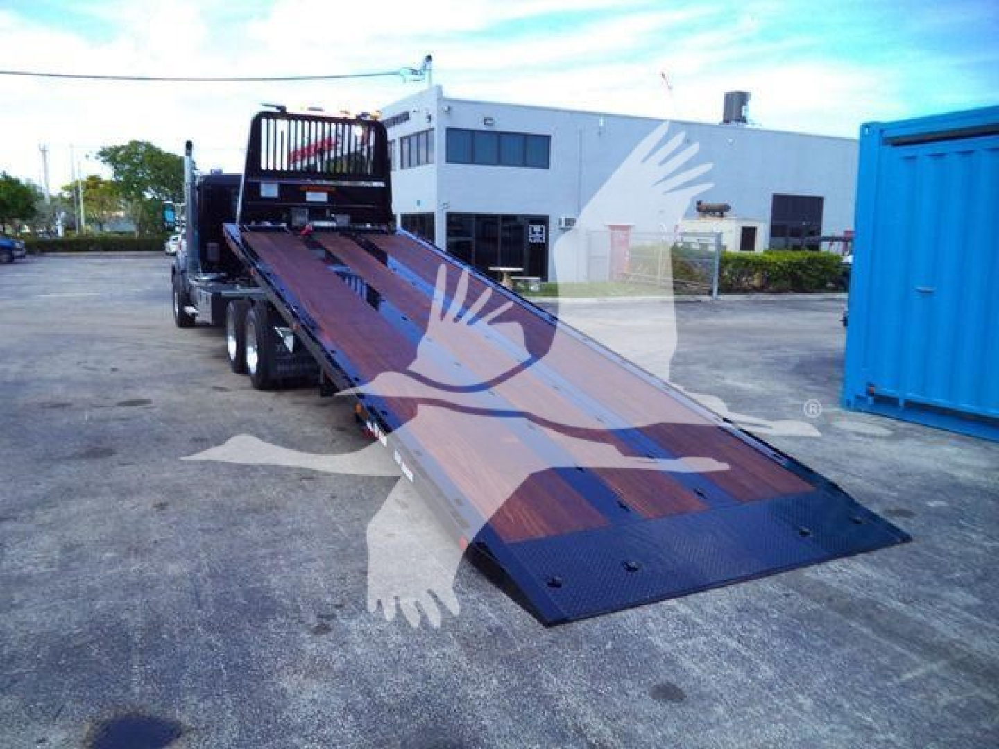 Tow truck with a long steel flatbed ramp loading area; Kenworth T880 front cab visible in background, blue ramp and rollback equipment.