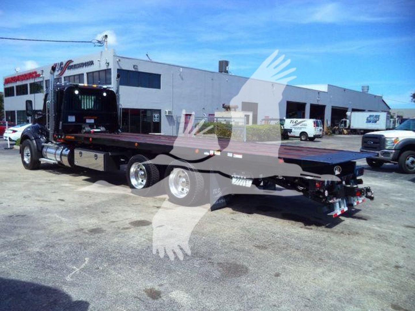 Kenworth T880 rollback truck on trailer in a dealership lot, side view showing long flatbed and rear hitch, with other trucks in background.