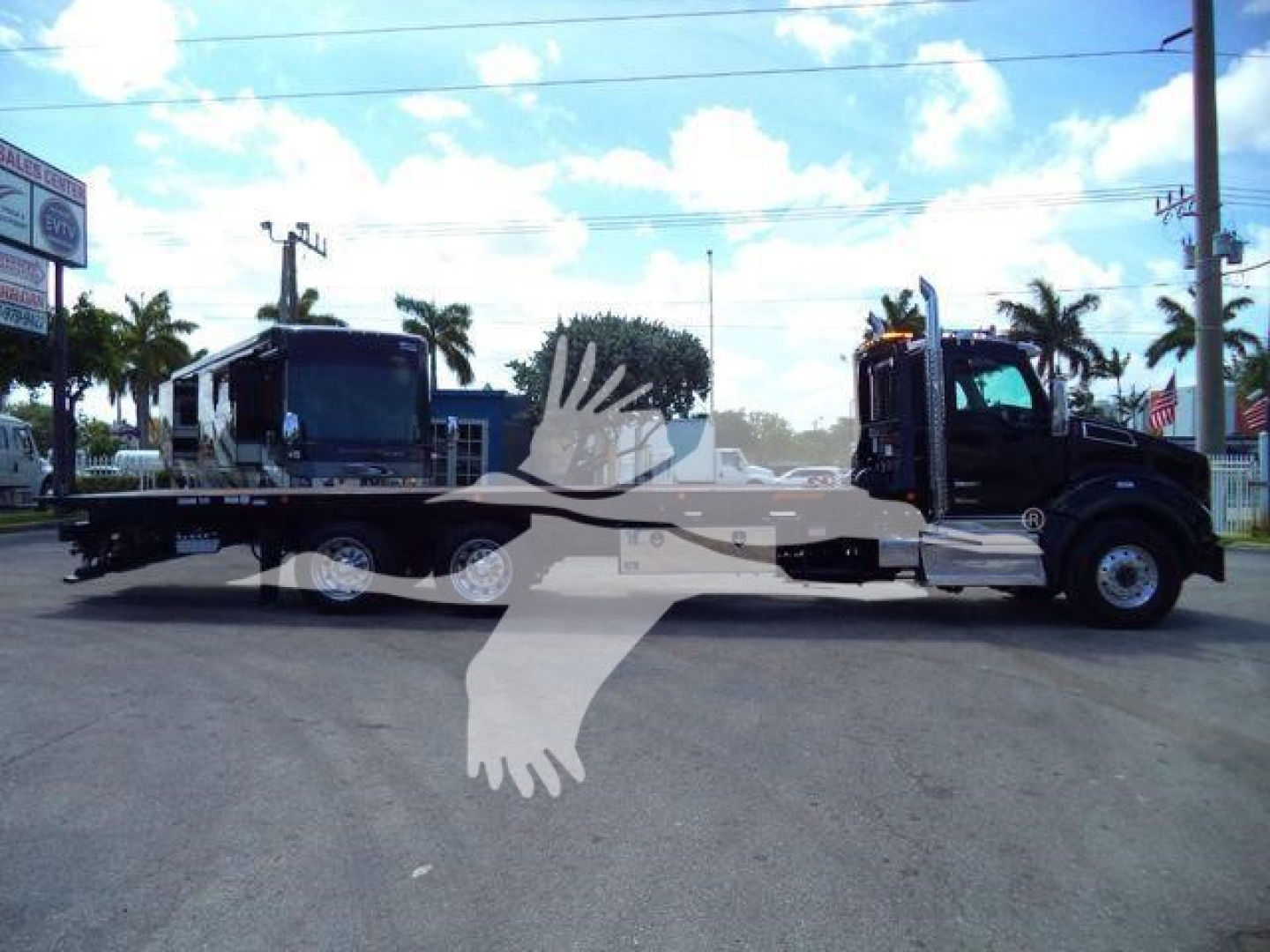 Kenworth T880 rollback truck with lowboy trailer in side view showing cab and trailer connection, dealership lot background with palm trees.