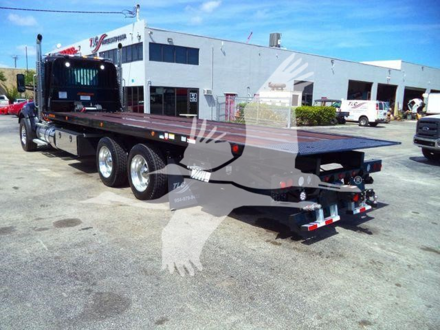 Kenworth T880 rollback truck with long flatbed and dual rear axles, rear view showing trailer hitch and rear lights.