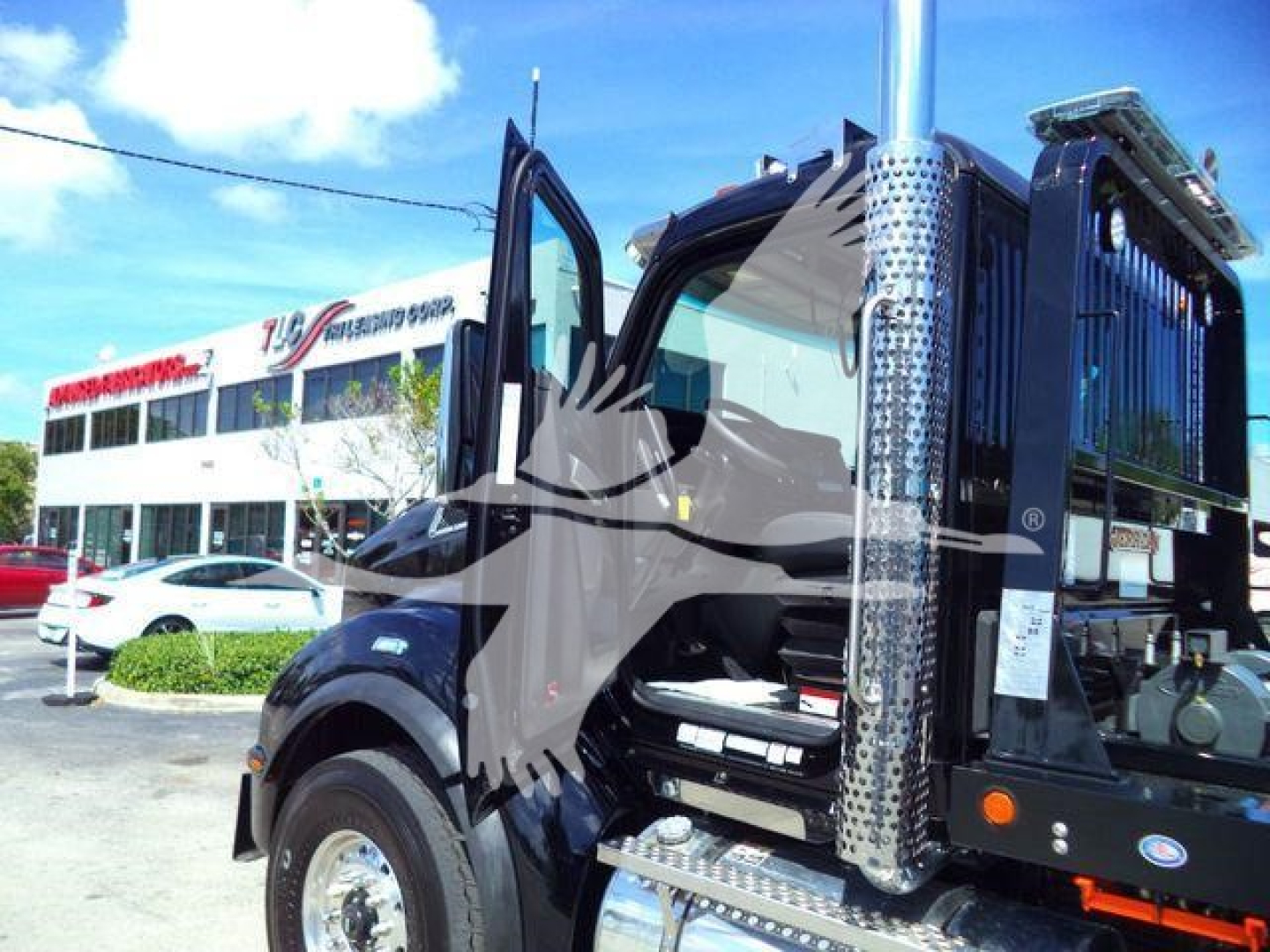 Kenworth T880 rollback truck cab with open doors showing chrome vertical exhaust and steps, dealership lot in background.