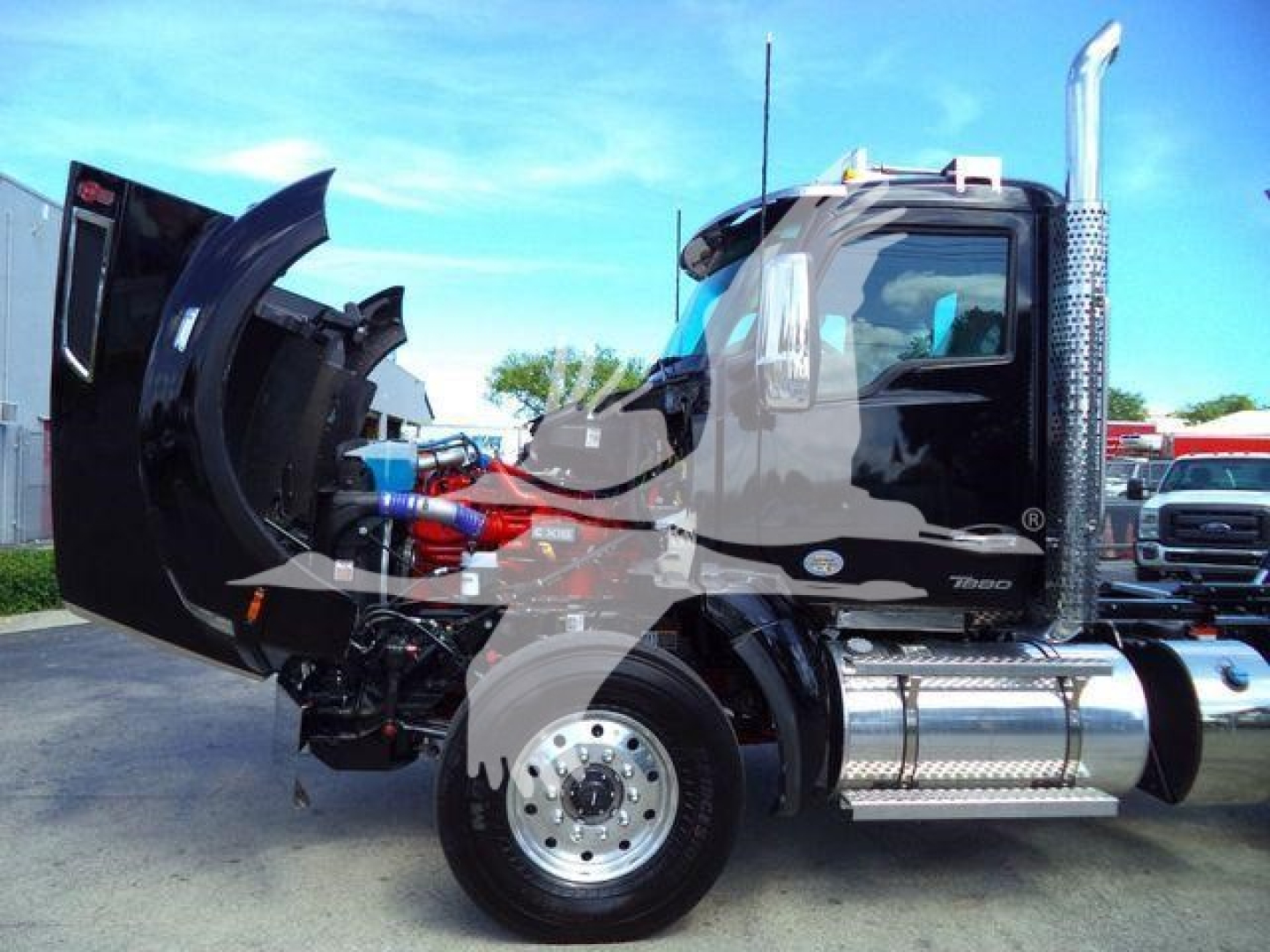 Kenworth T880 truck cab with hood open showing engine bay and chrome fuel tanks, rolling chassis and front wheel.