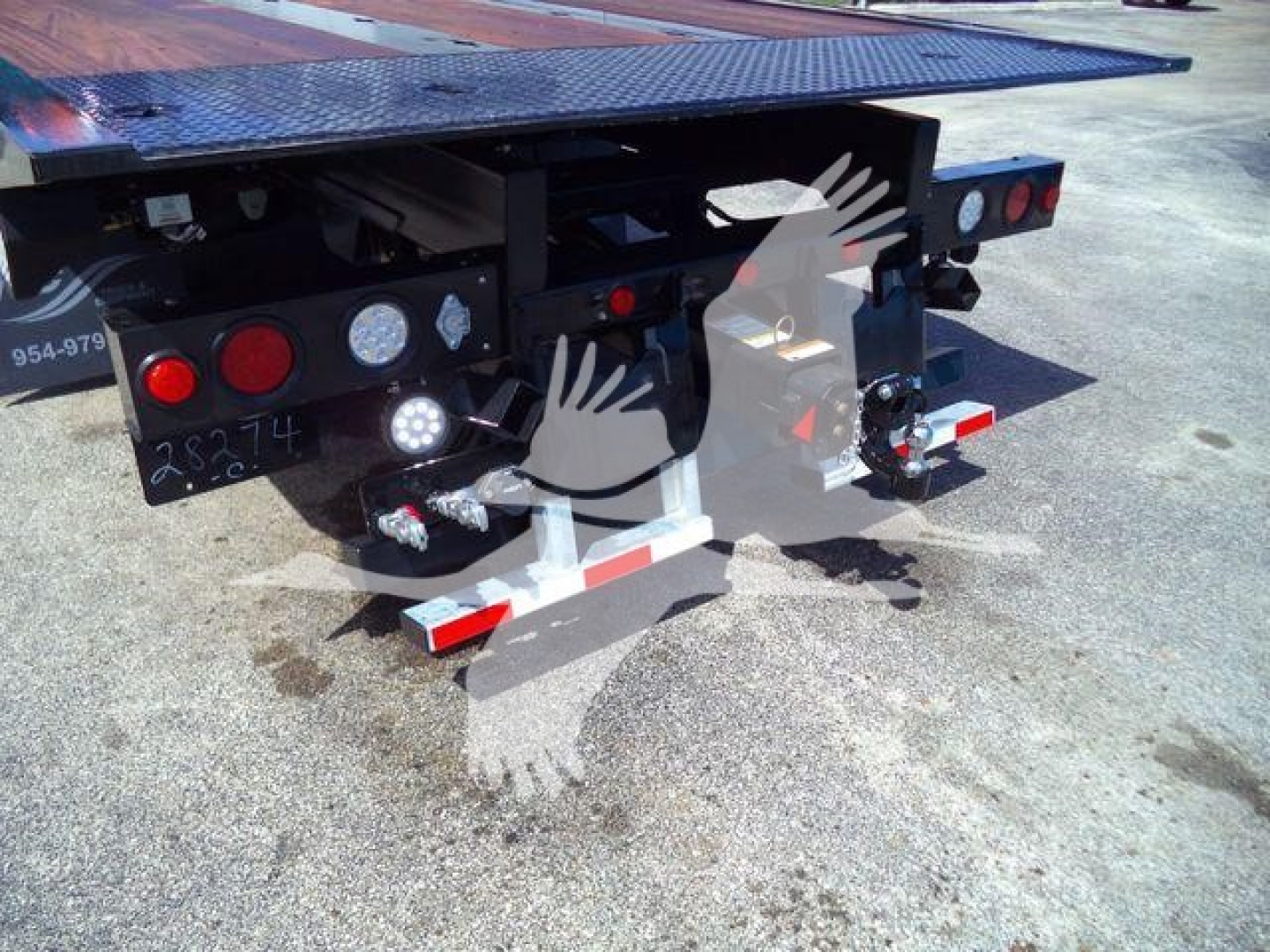 Rear view of a flatbed trailer hitch on a Kenworth T880 rollback truck showing tail lights, hydraulic hoses, and reflective red/white safety stripes.